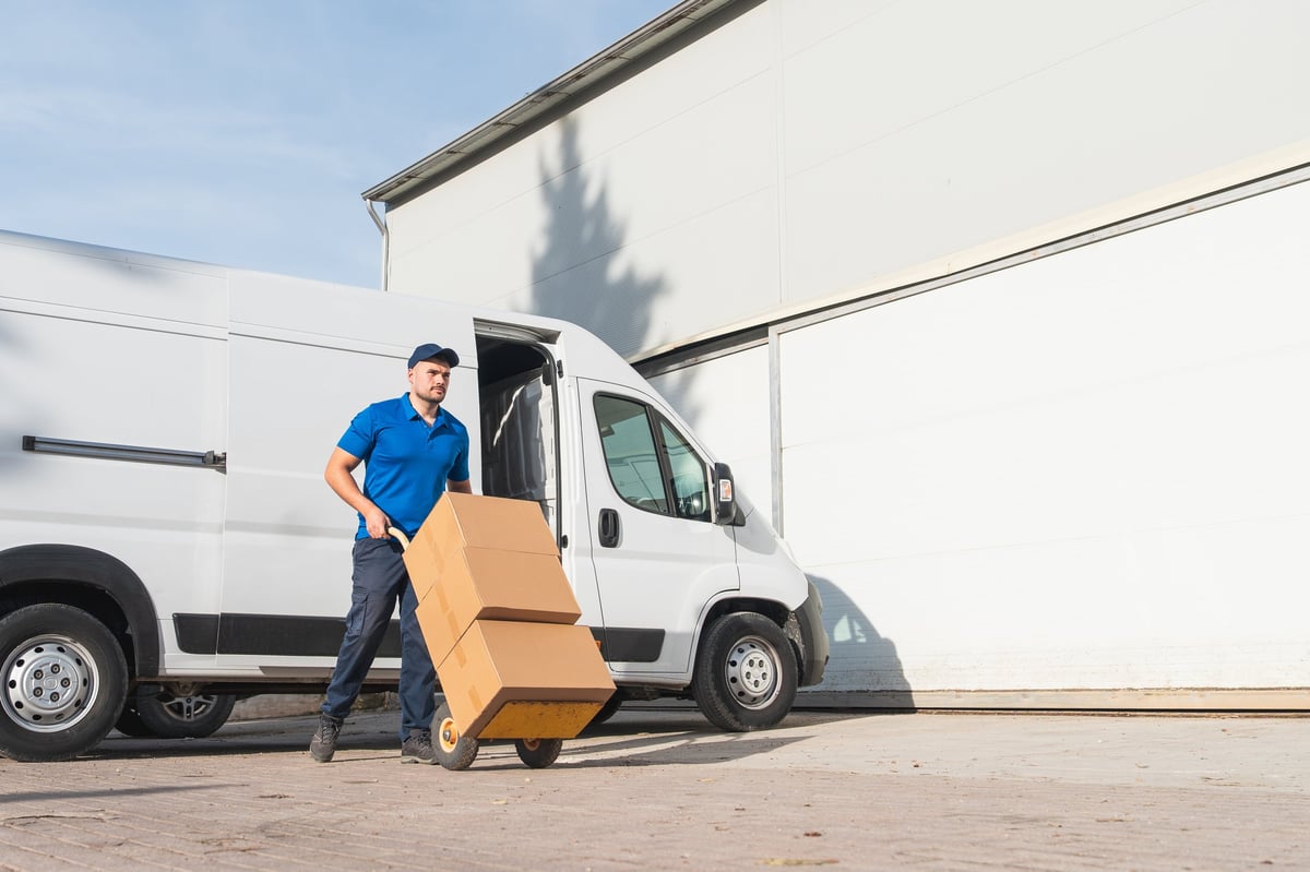 AJW delivery driver in uniform transporting boxes with a hand truck