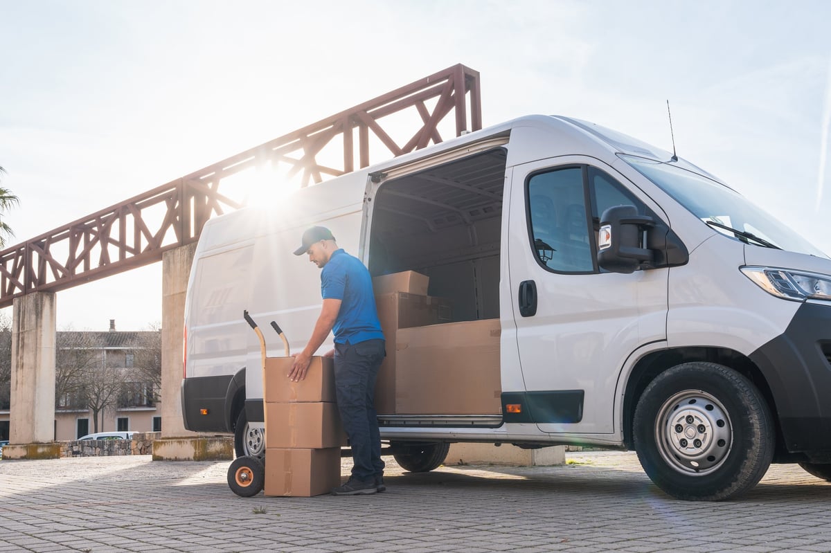 Delivery driver loading cardboard boxes into a van during golden hour